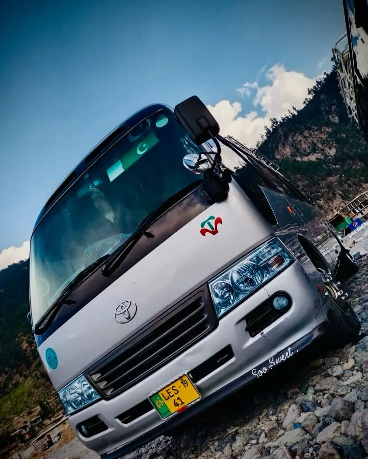 A Coaster parked on a hillside road